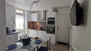 Eine kleine Küche mit weißen Schränken, einer Mikrowelle, einem Backofen und einem Essbereich mit Tisch für zwei Personen.