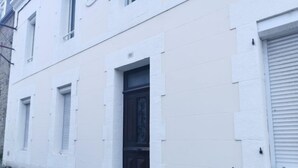 Ein weißes Gebäude mit einer dunklen Tür und Fenstern mit Rollläden.