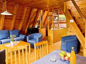 A cozy attic room with wooden beams, a sofa, a chair, a table with a glass and fruit, and a TV. - Geesthof by Interhome (Hechthausen)