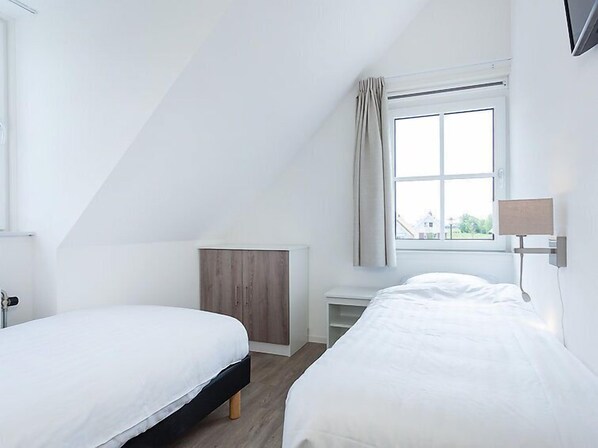 Un dormitorio con dos camas, una ventana con cortinas, un radiador y una lámpara de noche.