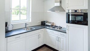 A modern kitchen with white cabinets, a gas stove, an oven, and a window providing natural light. - Vacation home Alk 8 by Interhome (Noordwijk)