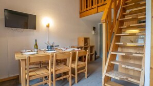 Un comedor con mesa y sillas de madera, televisor montado en la pared y una escalera de madera.