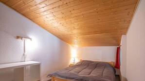 Un dormitorio con techo inclinado, una cama, una mesita de noche y una lámpara fijada a la pared.