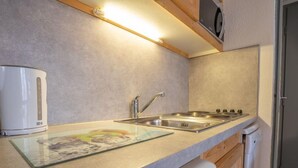 Una cocina compacta con un lavamanos de acero inoxidable, una estufa integrada y una tetera.
