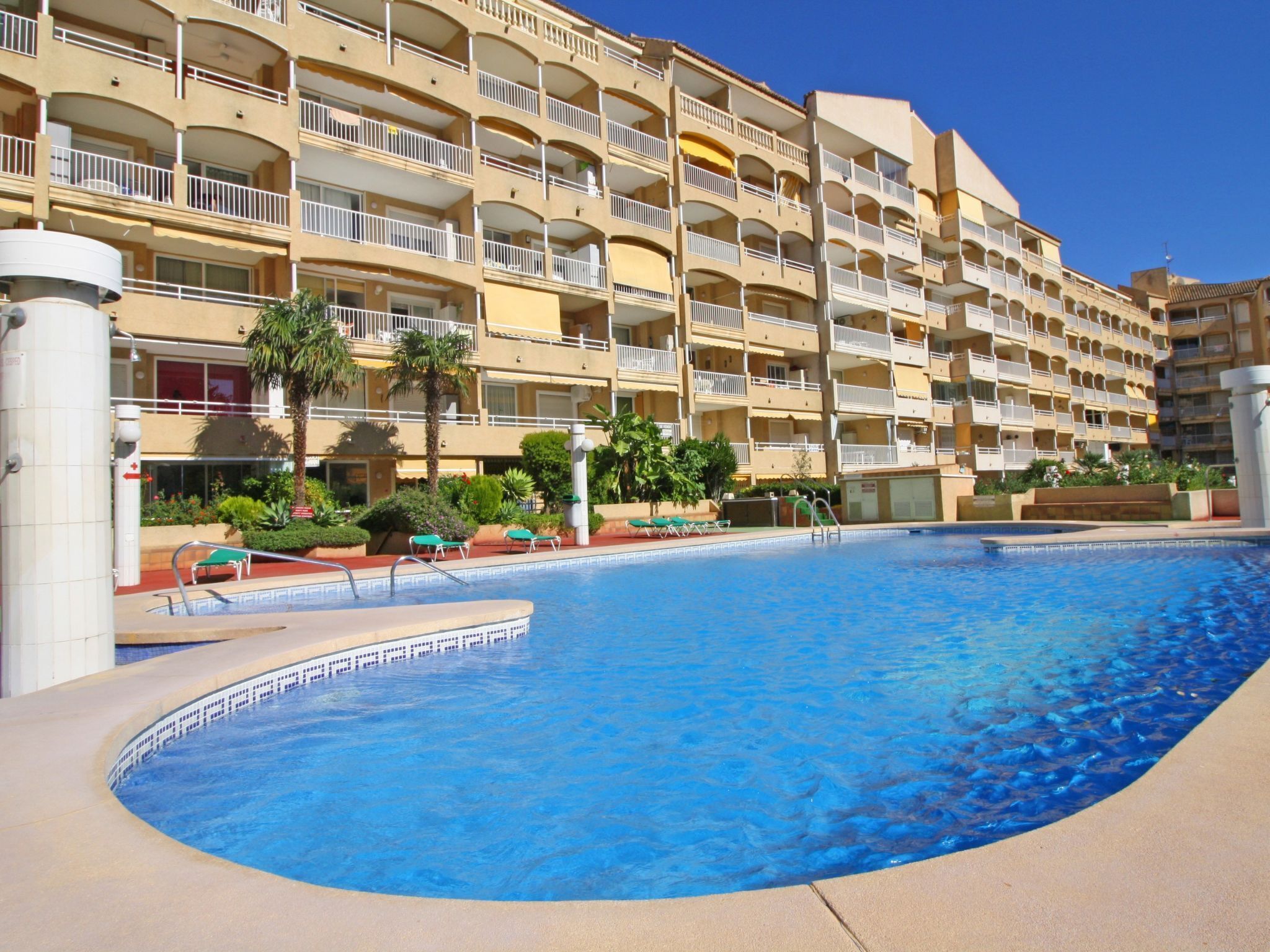 A hotel with multiple balconies, a swimming pool, and a landscaped garden area.