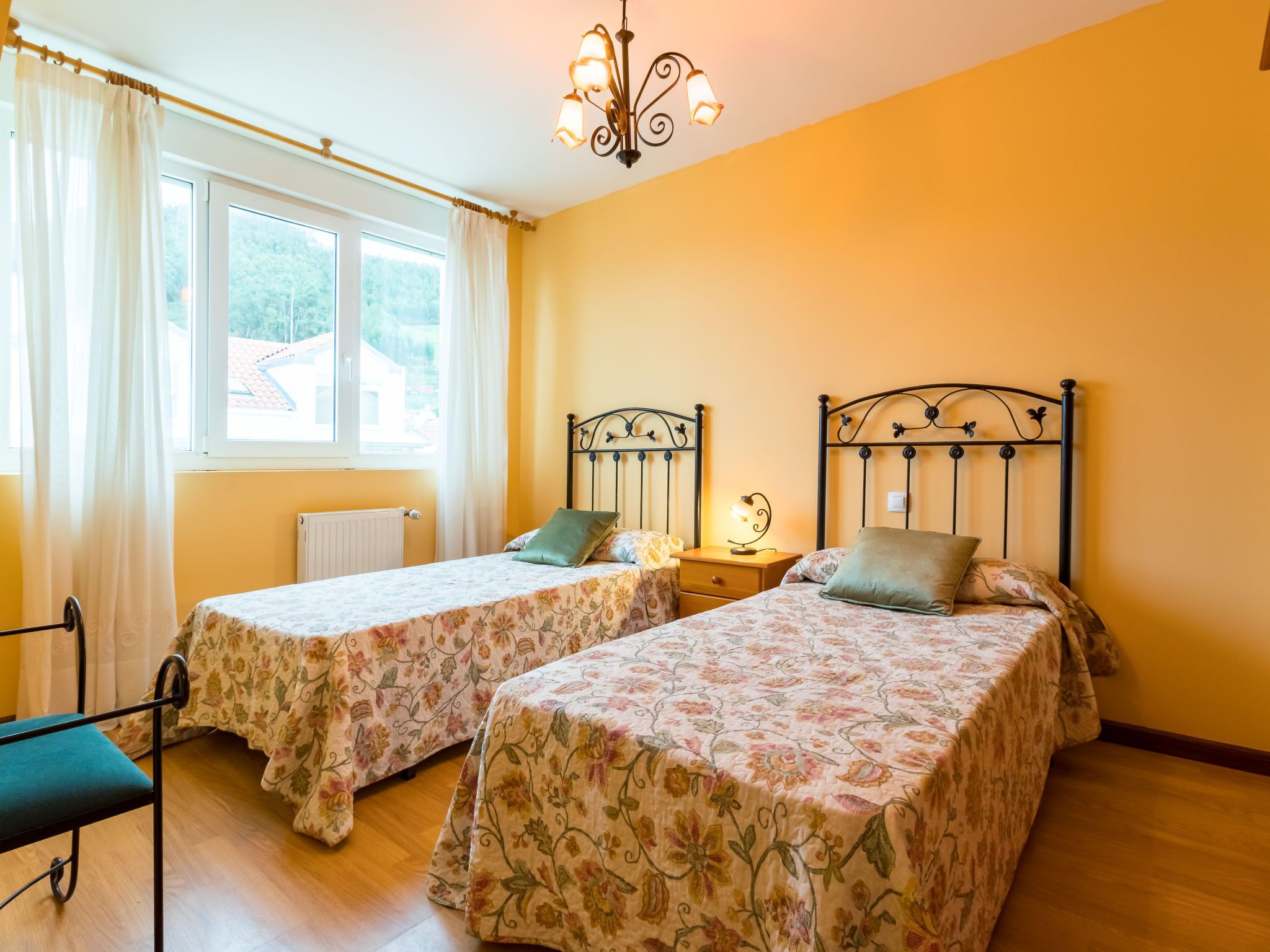 Una habitación con dos camas, una ventana con cortinas, un radiador y una mesita de noche con lámpara.