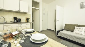 Una cocina moderna con armarios blancos, una mesa de comedor con platos y vasos, y un sofá con un cojín que dice 'Home is where the heart is'.