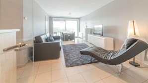 Ein modernes Wohnzimmer mit einer Couch, einem Sessel, einem Fernseher und einem Essbereich mit Tisch und Stühlen.