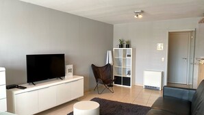Ein modernes Wohnzimmer mit Flachbildfernseher, einem weißen Schrank, einer Ledersofa, einem schwarzen Sessel, einem weißen Beistelltisch und einer Vitrine mit dekorativen Accessoires.