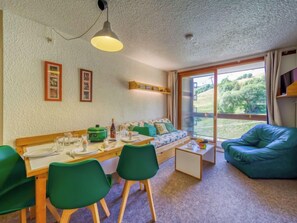 A cozy room with a dining table set for four, a sofa, and a large window offering a view of greenery.