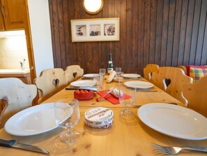 A wooden dining table set with plates, glasses, a bottle, and a red box of Le Rustique cheese.