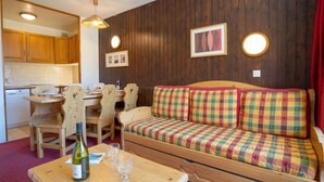 A cozy room with a wooden sofa, a dining table with chairs, a kitchen area, and a wooden cabinet.