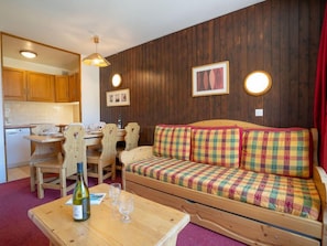 A cozy room with a wooden sofa, a dining table with chairs, a kitchen area, and a wooden cabinet.