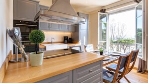 Een moderne keuken met grijze kastjes, een houten aanrechtblad en een groot raam met uitzicht op een balkon.