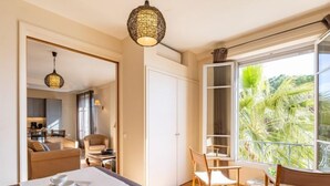 Een slaapkamer met een groot bed, een eethoek met stoelen, uitzicht op groen en een keuken op de achtergrond.
