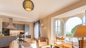 Een ruime woonkamer met een bank, stoelen, een salontafel en uitzicht op de omgeving door grote ramen.