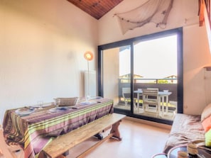 A room with a wooden table set for dining, a bench, and a sofa with a view to the outside.