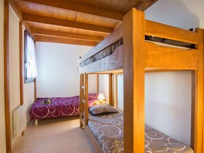 A room with two bunk beds, wooden beams on the ceiling, a window with curtains, and a radiator.