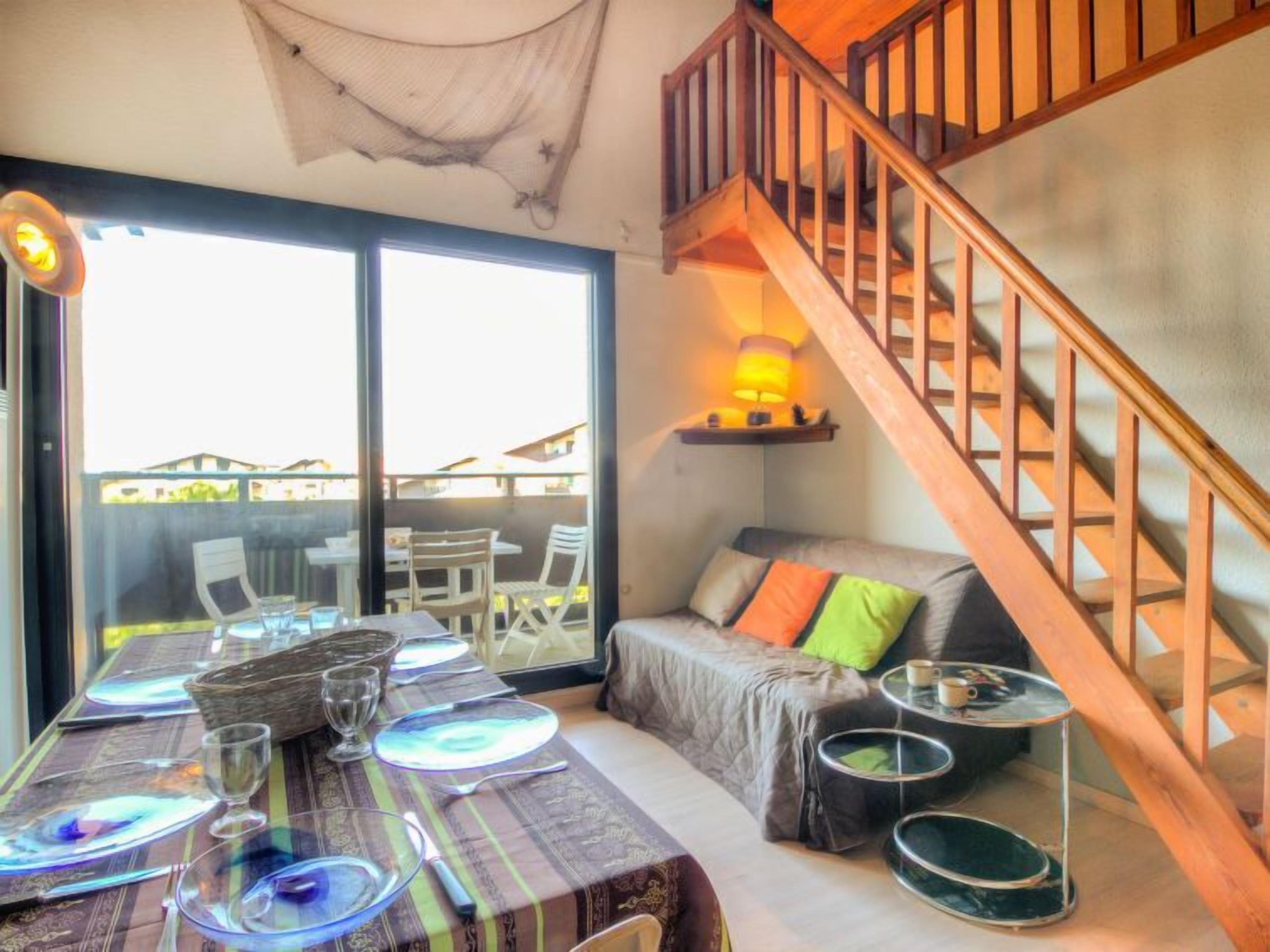 A dining area with a table set for four, a sofa with colorful cushions, and a wooden staircase.