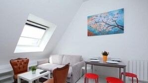 Ein modernes Wohnzimmer mit einer Couch, einem Esstisch mit Stühlen, einem roten Hocker, einem Gemälde und einem Oberlicht.