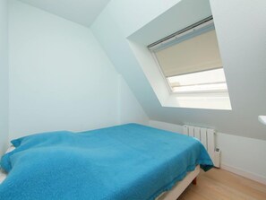 Een kleine kamer met een enkel bed, schuine wanden en een dakraam.