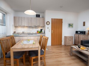 Une cuisine moderne avec des meubles en bois, une table à manger avec des chaises, une porte en bois et un petit coin salon avec une table et des chaises.
