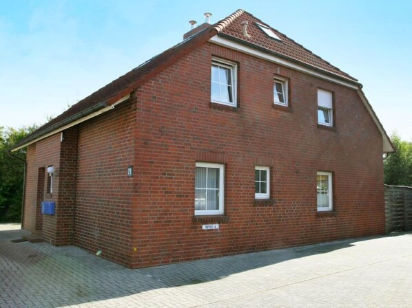 Une maison à deux étages, construite en briques, avec un toit en tuiles, un petit porche et une allée pavée.