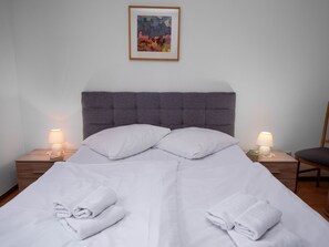 Un lit bien fait, avec du linge de lit blanc et des oreillers, deux lampes de chevet et un tableau encadré au mur.