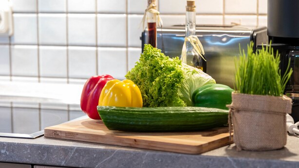 A kitchen counter with fresh vegetables, a cutting board, a bottle of oil, and a small potted plant. - Seehund by Interhome (Norddeich)