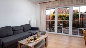 A modern living room with a grey sofa, wooden coffee table with food and drinks, and large windows overlooking a garden. - Seehund by Interhome (Norddeich)
