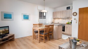A modern kitchen with wooden cabinets, a dining area with a table and chairs, a TV, and a small island with a sink and a wine glass. - Seehund by Interhome (Norddeich)
