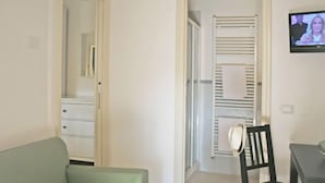 Een kamer met een groene bank, een eettafel met twee stoelen, een televisie aan de muur en een witte garderobe met spiegel.