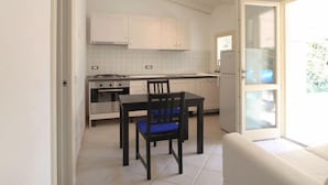 Een compacte keuken met witte kastjes, een eettafel met stoelen en een inbouwoven.