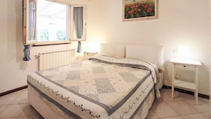 Een slaapkamer met een bed, een nachtkastje, een raam met gordijnen, een radiator en een schilderij aan de muur.