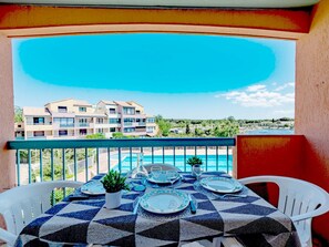 Une table à manger dressée pour quatre personnes, avec vue sur un bâtiment et une piscine.