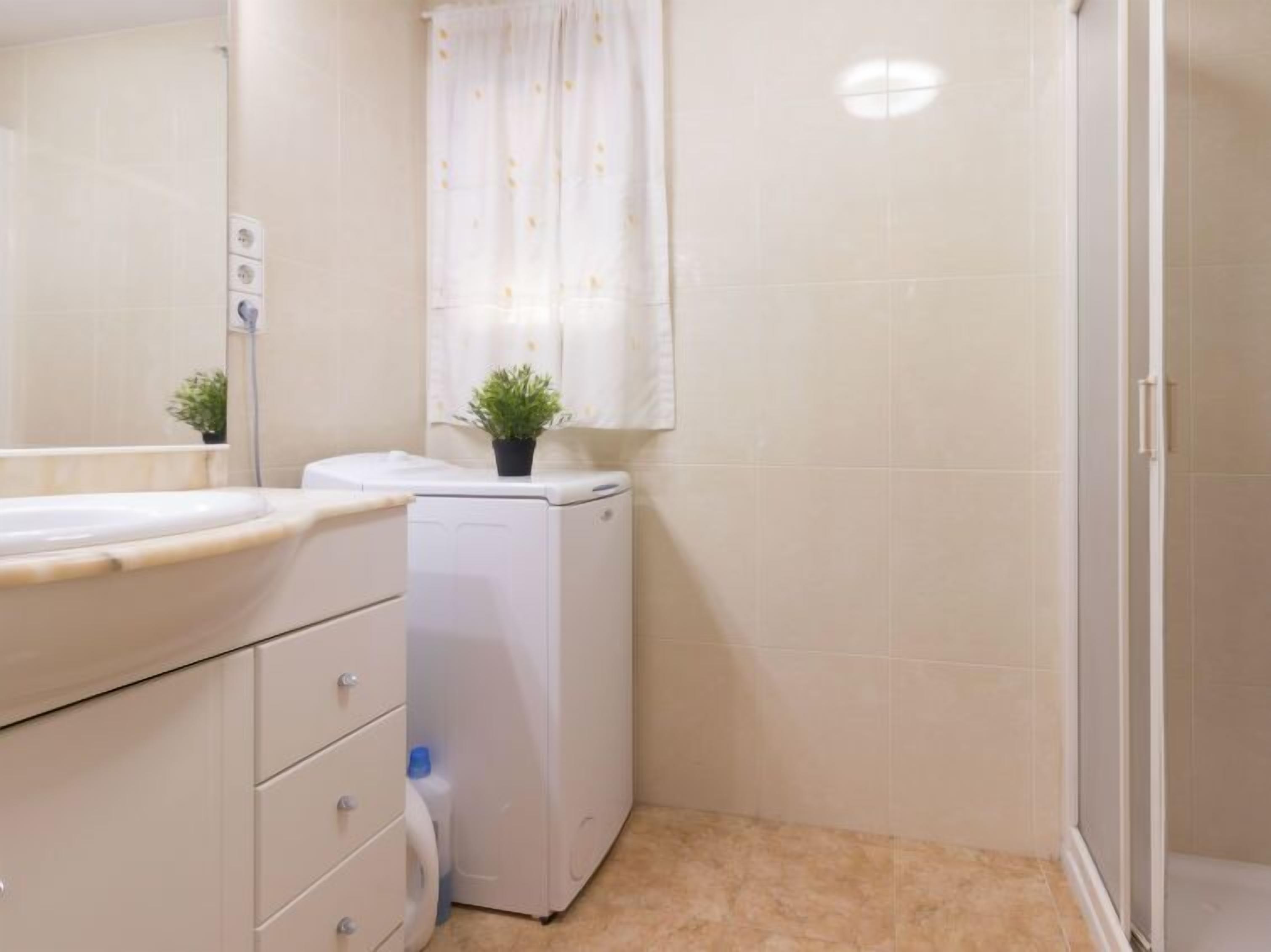 A small bathroom with a sink, a washing machine, and a shower.