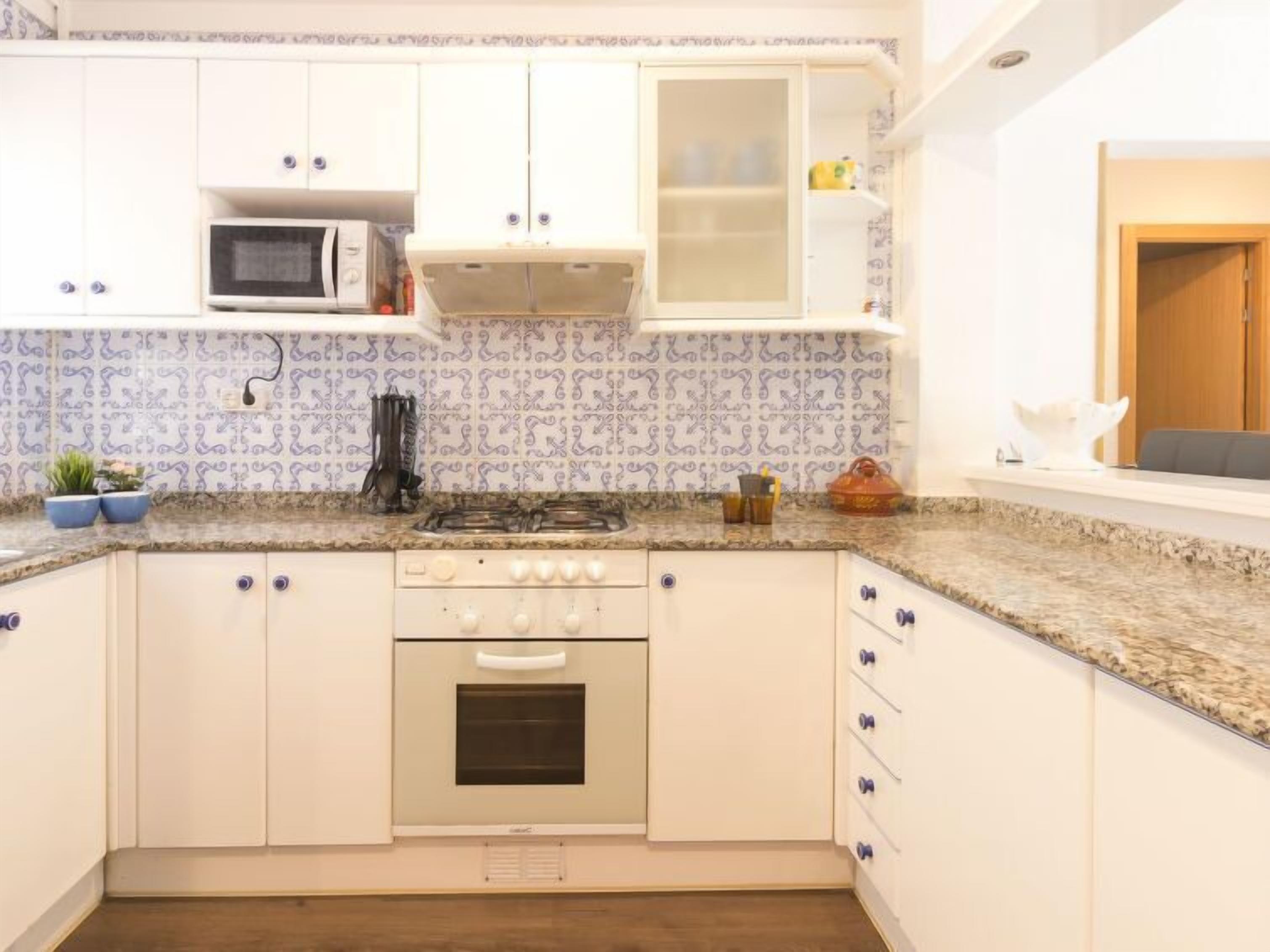 A kitchen with white cabinets, a microwave, a stove, and a sink.