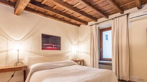 Ein Schlafzimmer mit Holzboden, einem Bett mit weißer Bettdecke, einem Nachttisch mit Lampe und einem Fenster mit Vorhängen.