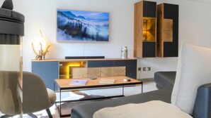 Un salon moderne avec un téléviseur à écran plat fixé au mur, une table basse en bois, un canapé gris et un fauteuil noir.