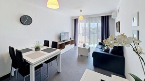A modern living room with a dining area, a sofa, a TV, and a clock on the wall. - Port Banyuls by Interhome (Empuriabrava)