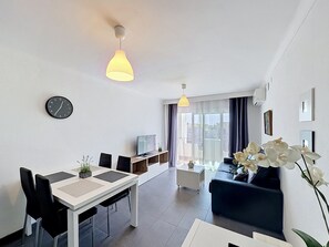 A modern living room with a dining area, a sofa, a TV, and a clock on the wall.