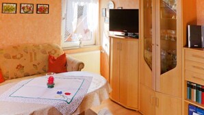 Una camera accogliente con un divano, un tavolo con tovaglietta, una televisione su un mobile e una finestra con tende.