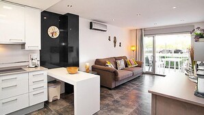 A modern kitchen with white cabinets, a black accent wall, and a dining area with a brown sofa and a small table. - Apartment DMS V by Interhome (Cambrils)