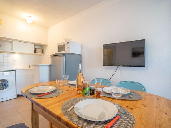 A dining area with a wooden table set for two, a microwave, a washing machine, and a TV mounted on the wall. - Port Quiétude by Interhome (Fréjus)