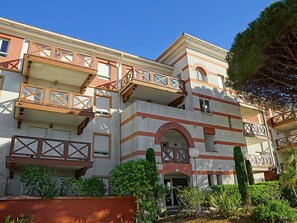 A multi-story building with balconies, a central archway, and surrounding greenery.