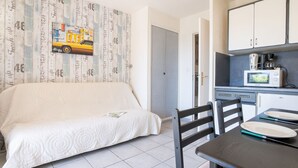 Una stanza compatta con un letto, un tavolino, una sedia, angolo cottura e una porta che dà su un'altra stanza.