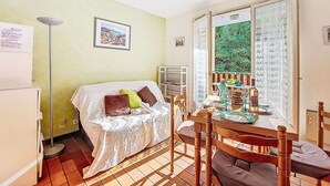 Una habitación pequeña y acogedora con una cama, una mesa con sillas, un radiador y una ventana con vistas a zonas verdes.