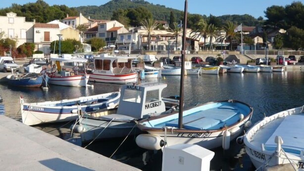 Un puerto deportivo con varias embarcaciones amarradas, rodeado de edificios residenciales y un paisaje montañoso.