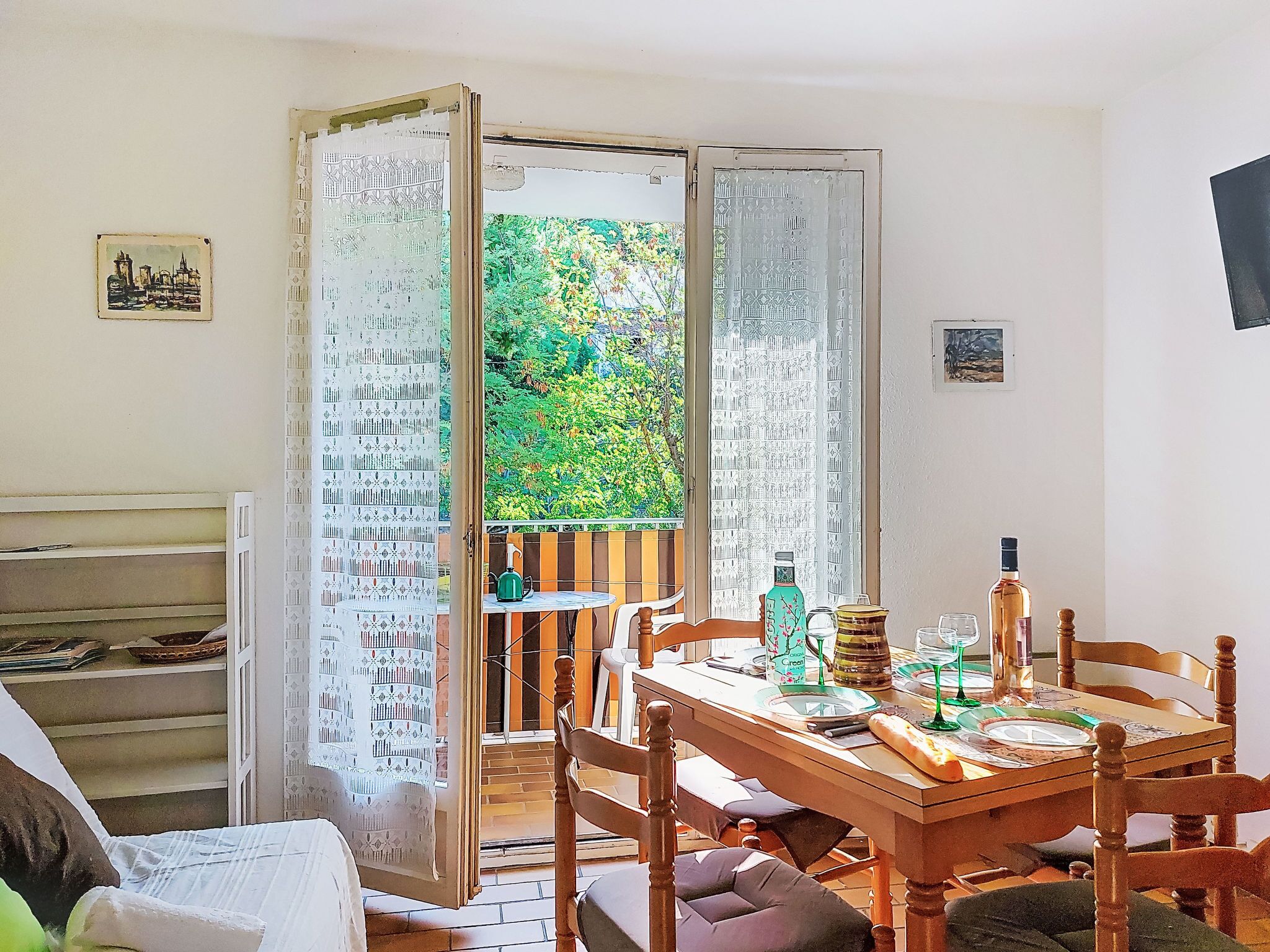 A dining area with a wooden table, chairs, and a view of greenery through open curtains.