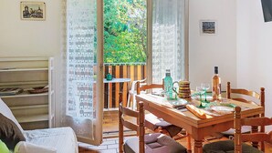 Un comedor con una mesa de madera, sillas y vistas a la vegetación a través de cortinas abiertas.